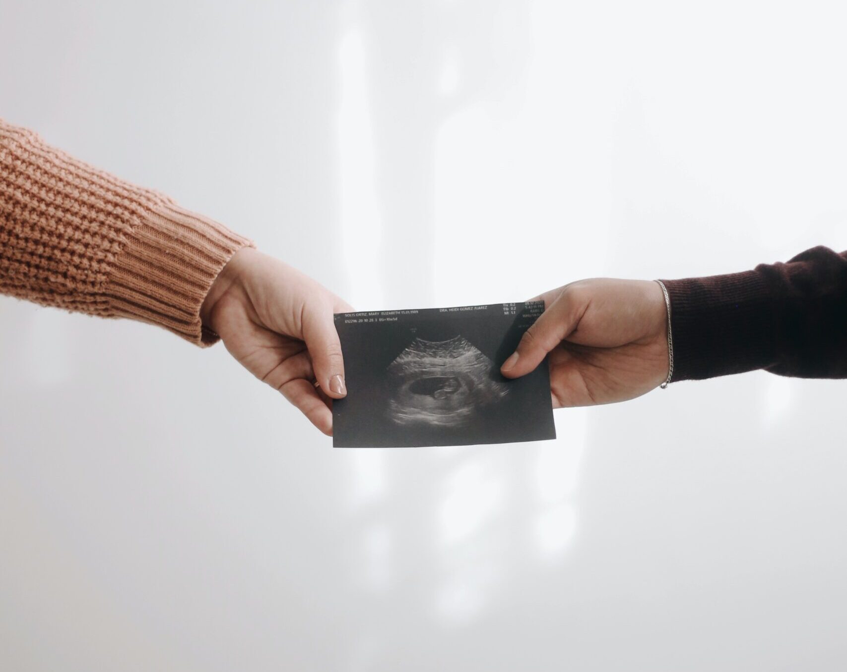 two individuals’ hands hold a pregnancy ultrasound