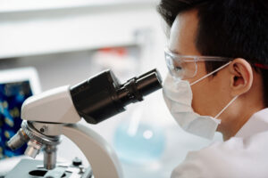 technician in lab coat looking through microscope